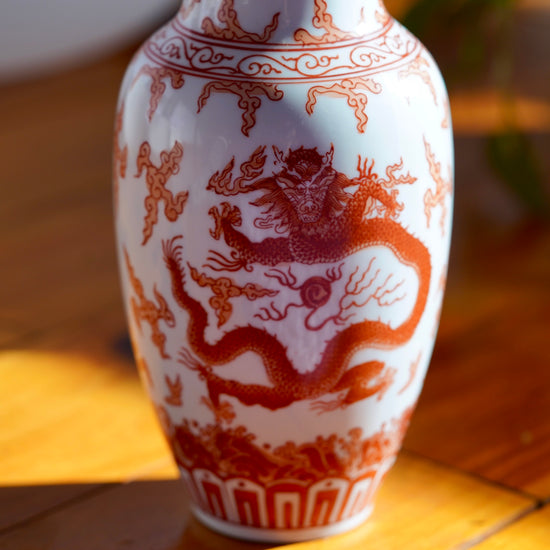 Macro photo of dragon painted on body of Vintage orange and white hand painted Japanese porcelain vase with  dragons, displayed on wood floor