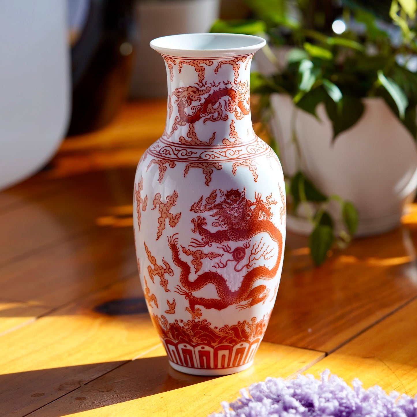 Vintage orange and white hand painted Japanese porcelain vase with  dragons, displayed on wood floor with potted plant in background