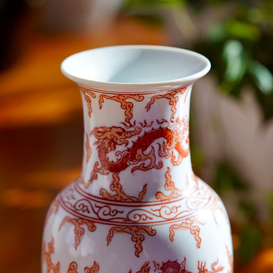 Close up photo of stem and rim of opening on vintage orange and white hand painted Japanese porcelain vase with  dragons, with potted plant in background