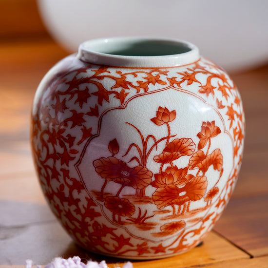 Vintage white and orange handpainted Japanese porcelain vase with flowers, displayed on light wood floor with purple rug in bottom left corner.