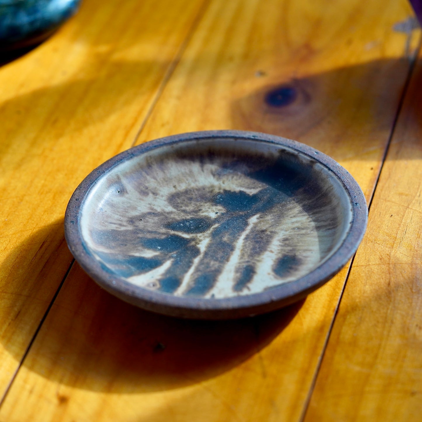 Distant photo of brown and white Moroccan inspired ceramic dish set on a light wood floor, with a labradorite crystal showing at the top left corner of the frame