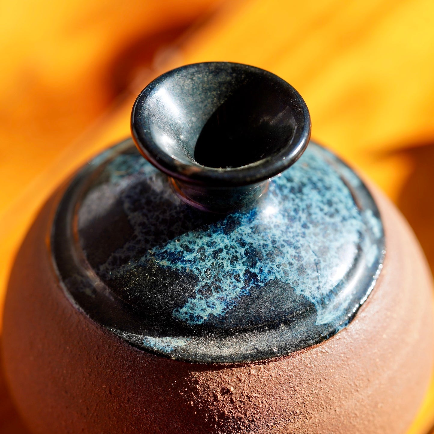 Close up shot of top rim and glaze on a handmade brown clay ceramic bud vase, displayed on a light wood floor