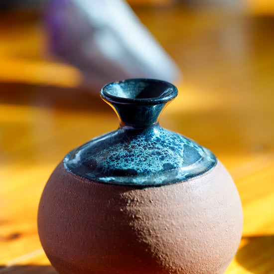 Load image into Gallery viewer, Close up photo of black, white, and blue nebula glaze on top of a handmade brown clay ceramic bud vase, displayed on a light wood floor

